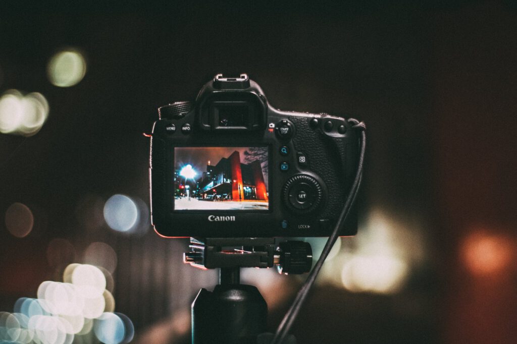 selective focus photography of black canon camera displaying photo of red and black building